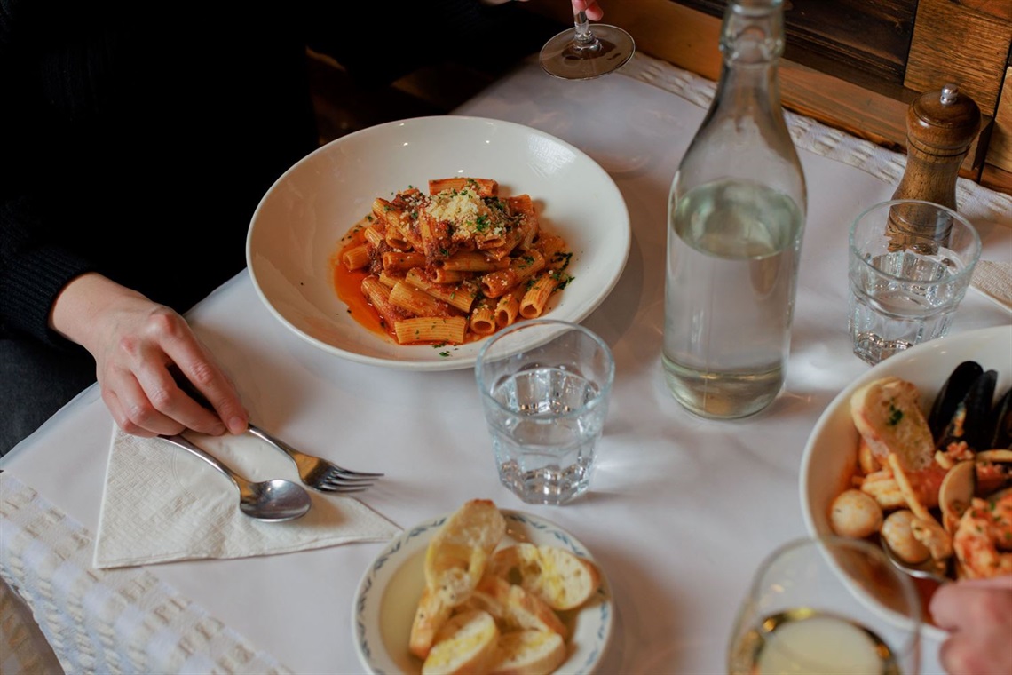  A table with a bowl of pasta, a bowl of clams, buttered bread, wine and water.