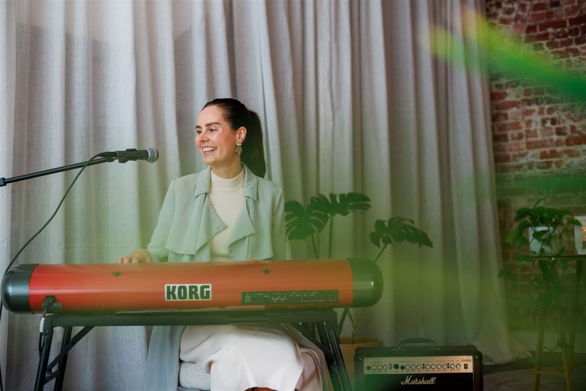 A smiling woman playing a keyboard on a stage with a curtain behind her.