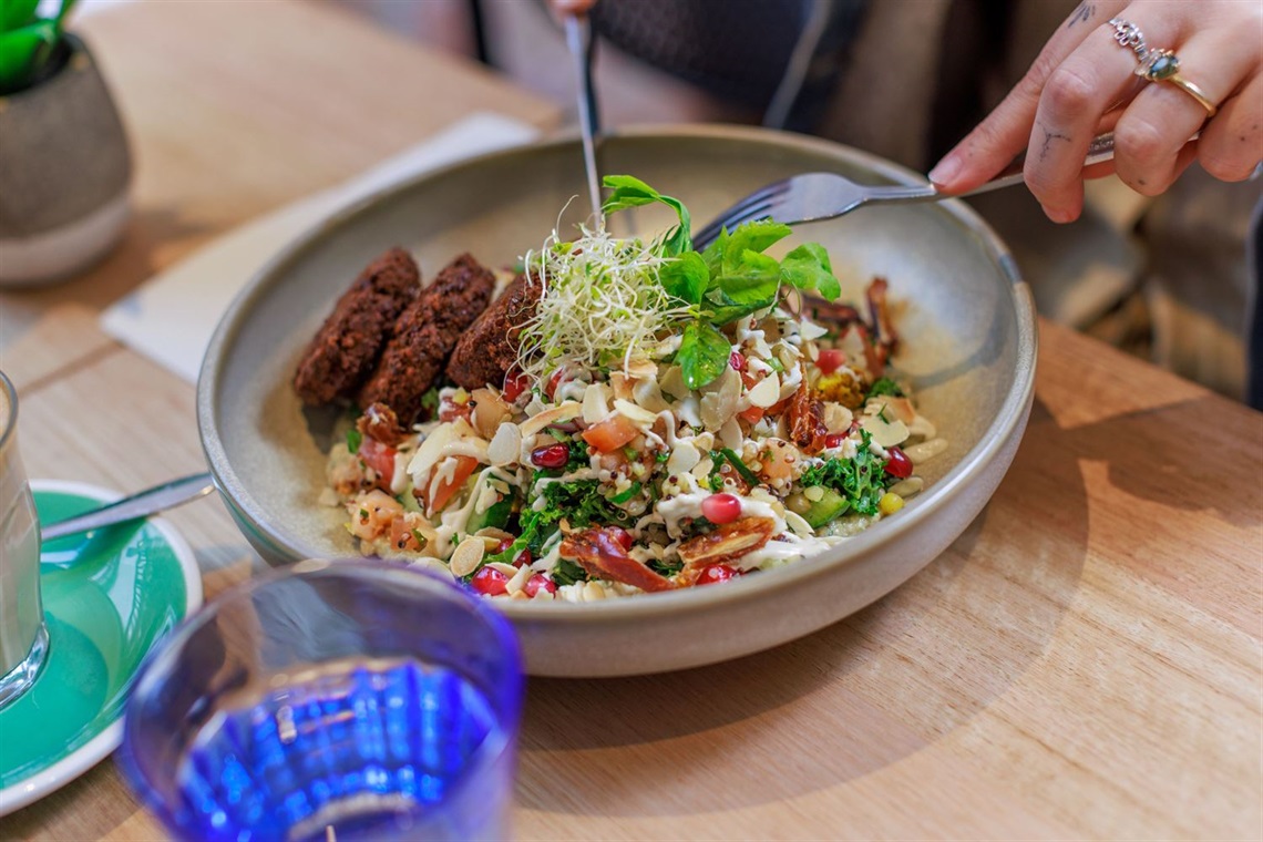  A bowl with salad and falafel patties. A woman's hands are holding cutlery. cutlery to 