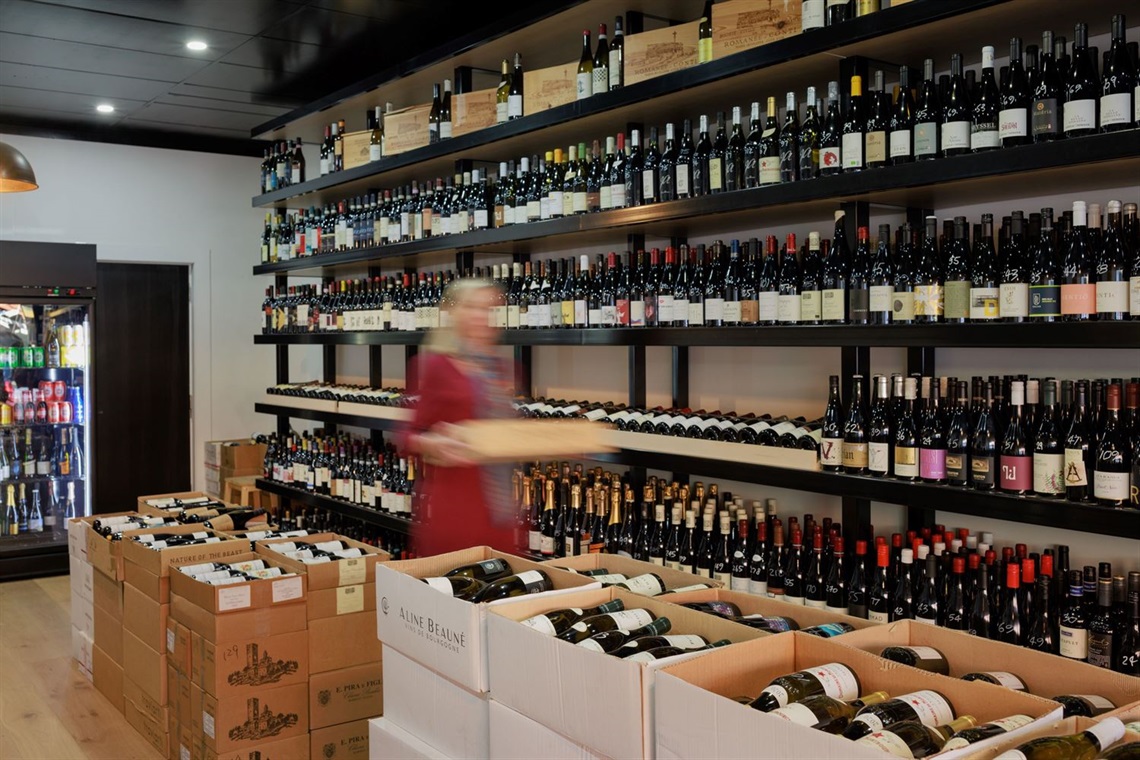 A room a large shelf filled with wines, open boxes of wines on the floor and a cool room with chilled wines.