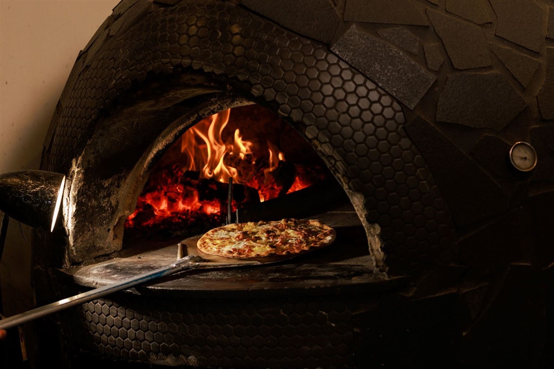 A woodfire pizza oven with a cooked pizza being taken out on a long baker's pole.