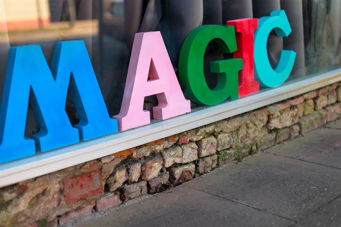 Large colourful wooden blocks spelling out the letters of the word MAGIC in a shop window., with a curtain behind them.