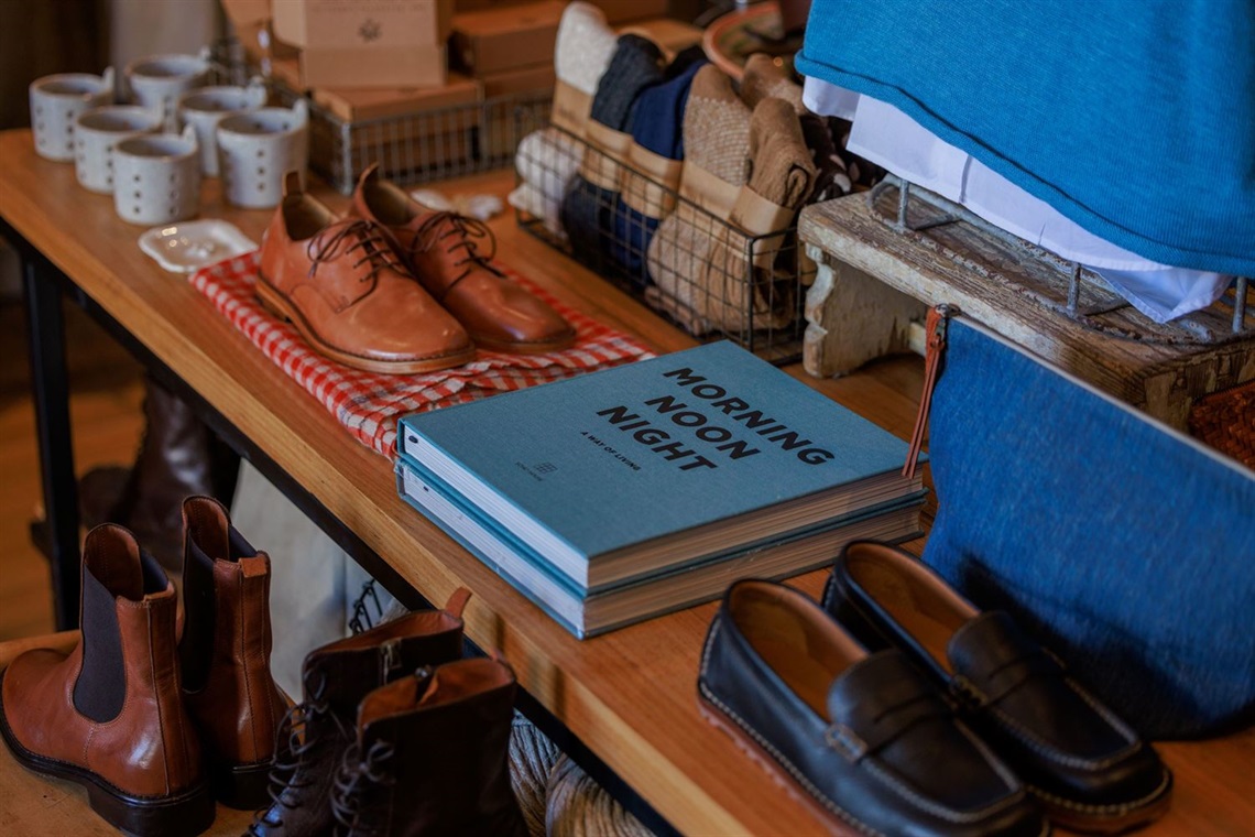 A wooden display table with leather shoes, books, socks, and ceramics on it.