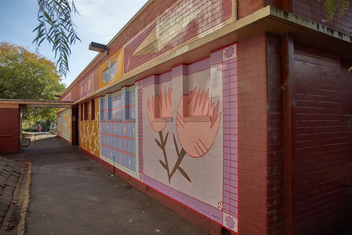 Mural on a brick wall showing flowers, bright colours and a earthy palette