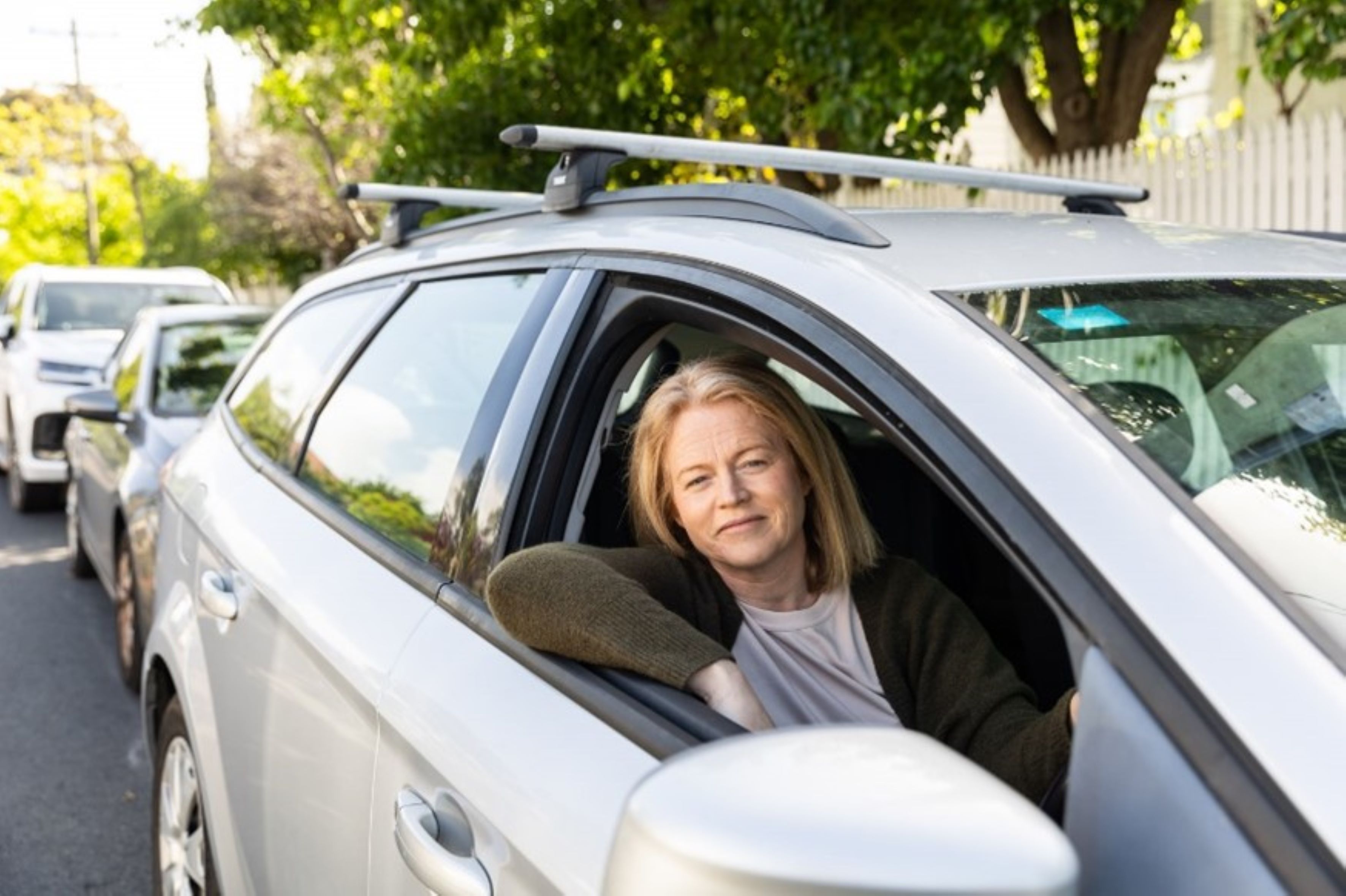 Woman in silver station wagon in a line of traffic.