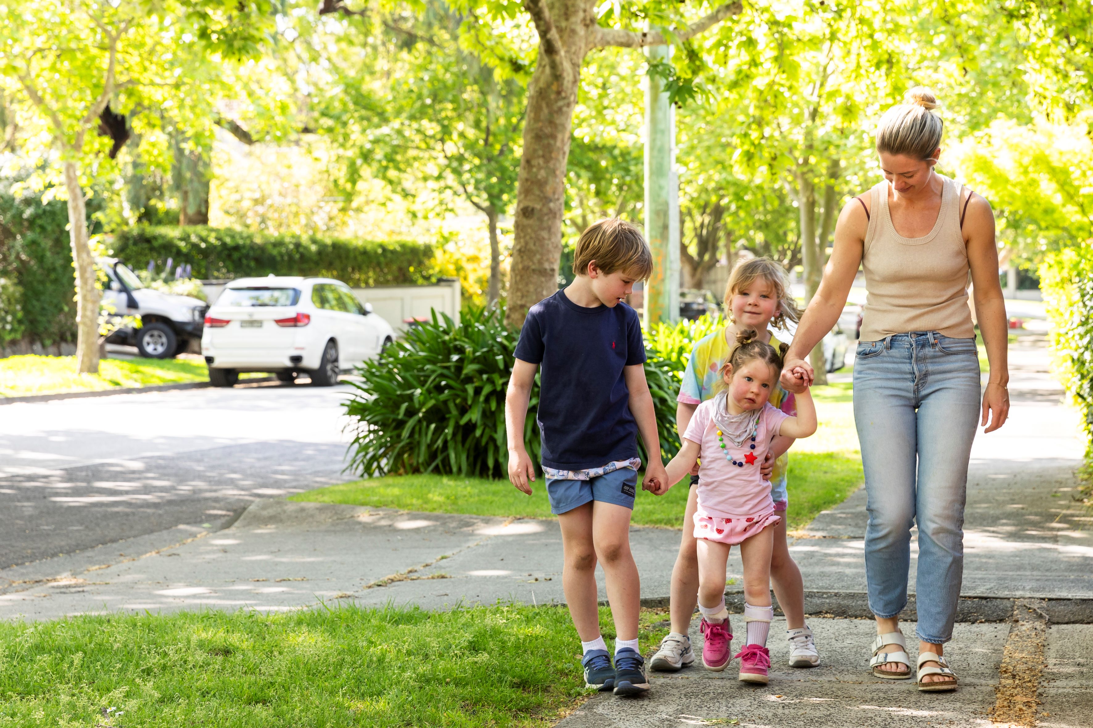 Woman and three children walking on residential street. There are green trees in the background.