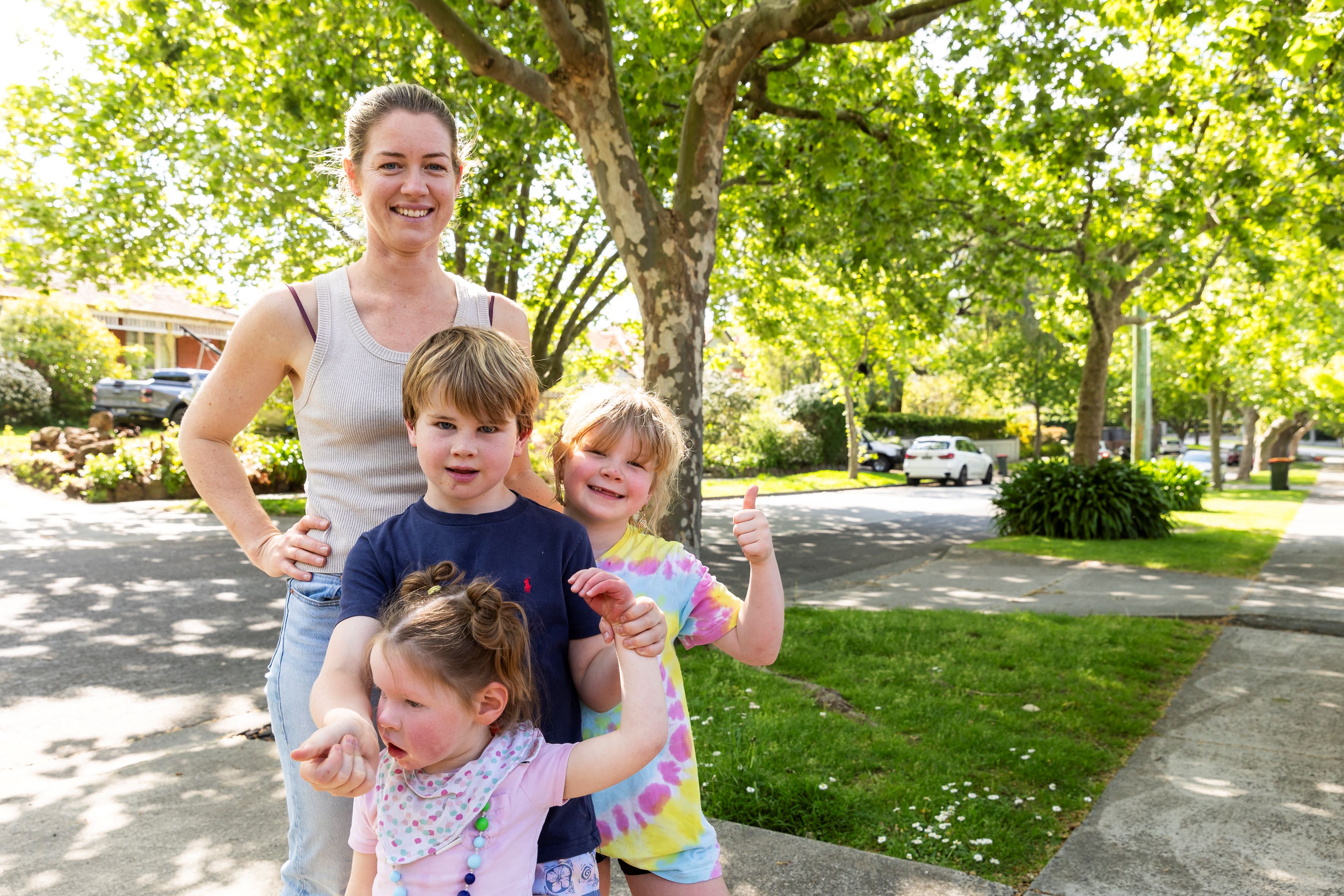 Woman and three children standing in residential street with green trees in background.