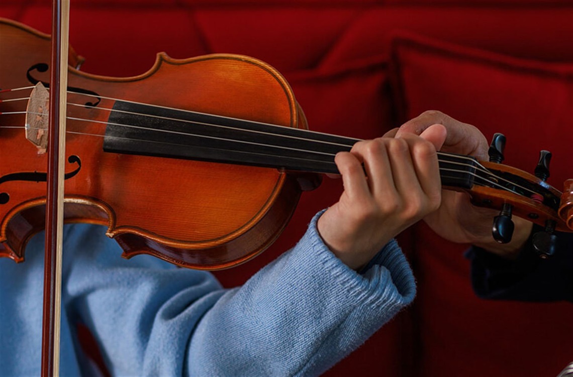 Man and child sitting on a red couch playing the violin.  A saxaphone, guitar and viola sit next to the couch