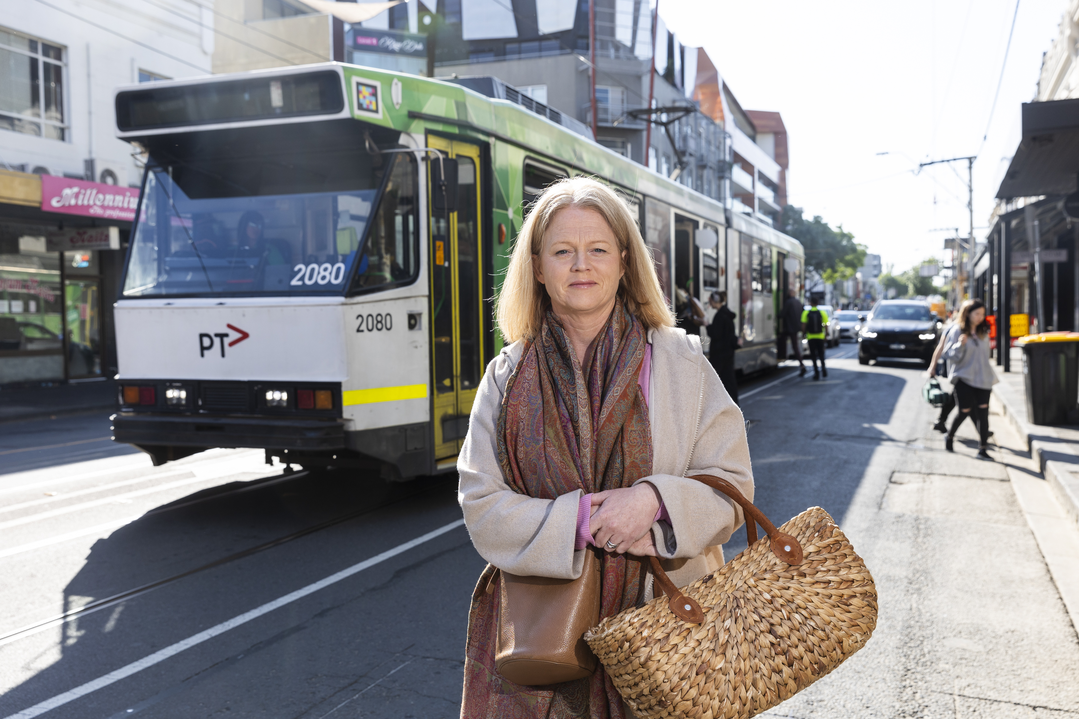 Person standing at tram stop with a tram in the background.