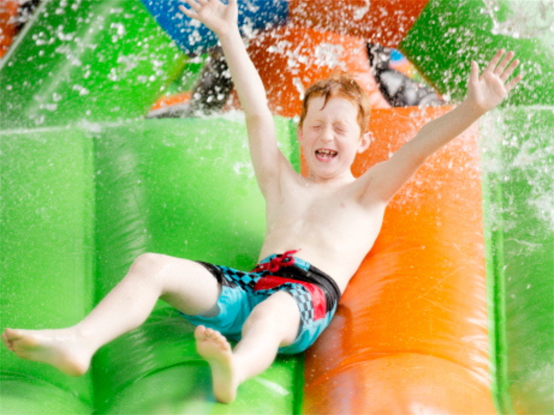 young child sliding down green and orange inflatable slide with hands in the air